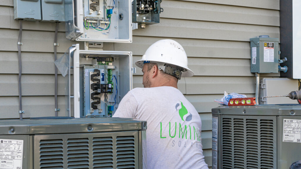 Lumina Solar electrician in a hard hat, performing electrical services on the side of a home.