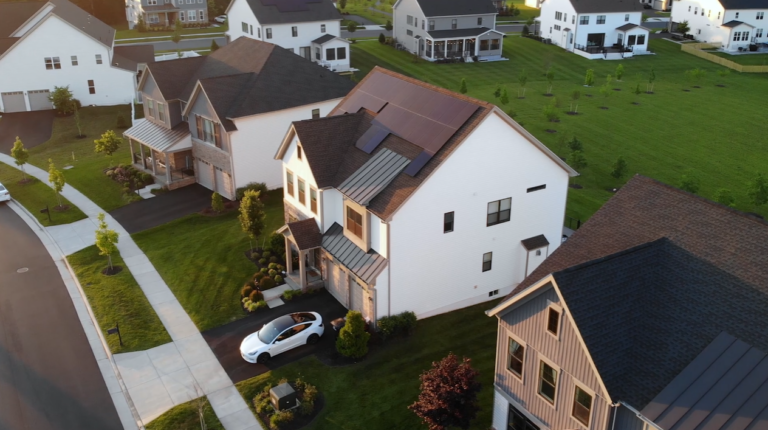 Single family home with all-black solar panels on a black shingle roof with an electric vehicle in the driveway in front of the home