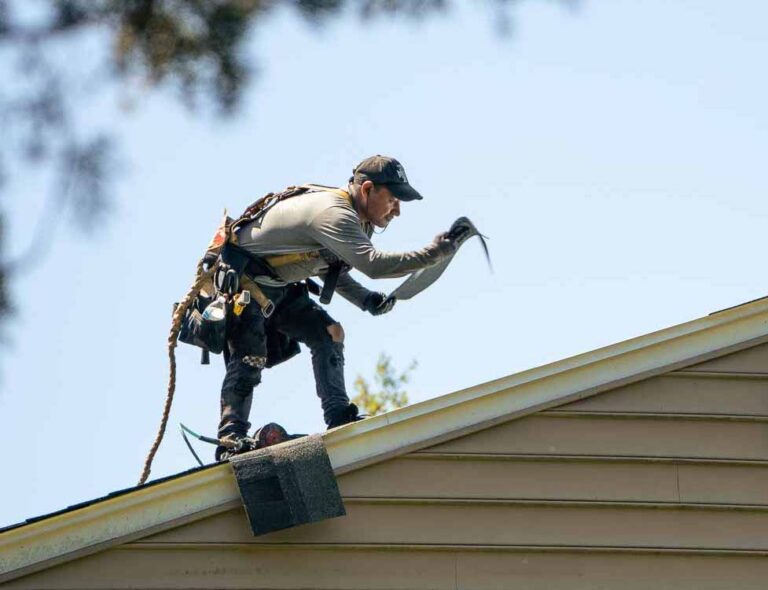 A roofer laying roof shingles on a home