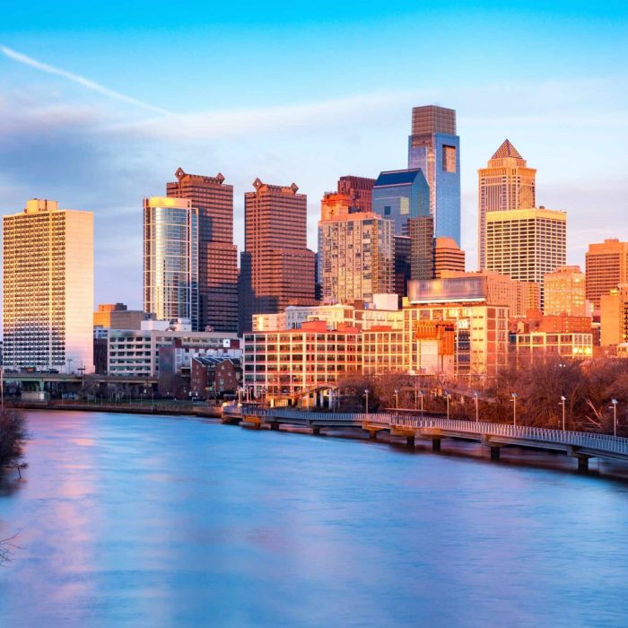 Late afternoon in Philadelphia.  The skyline glows under an orange sunset light. Schuylkill expressway traffic runs parallel to Schuylkill river.